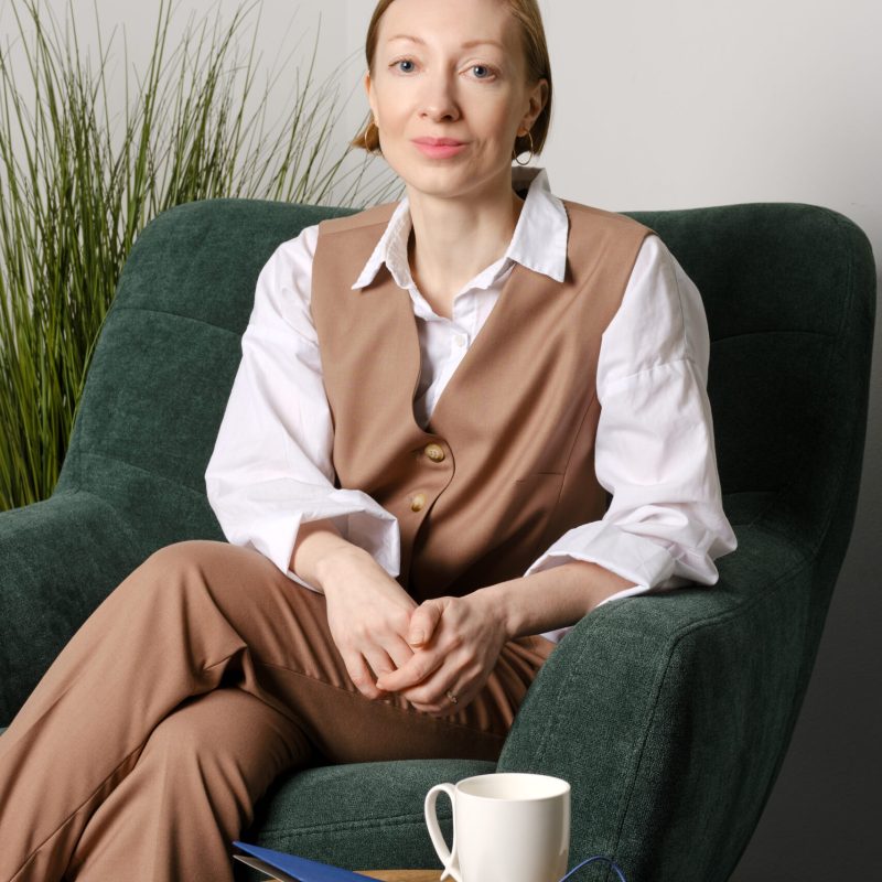 Portrait of cheerful young adult woman sitting in cosy armchair in office rest room